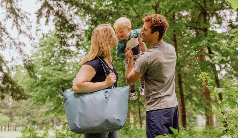 mom holding insulated cooler bag while dad plays with his young son while out on a hike