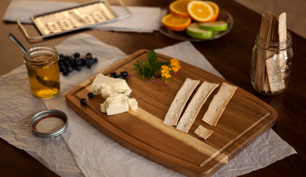 cutting board on table with cheese, crackers, fruit and honey