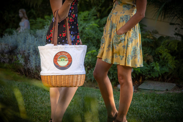Two women in garden wearing summer dresses, one holding wicker tote with “The Child,” casual cheerful vibe.