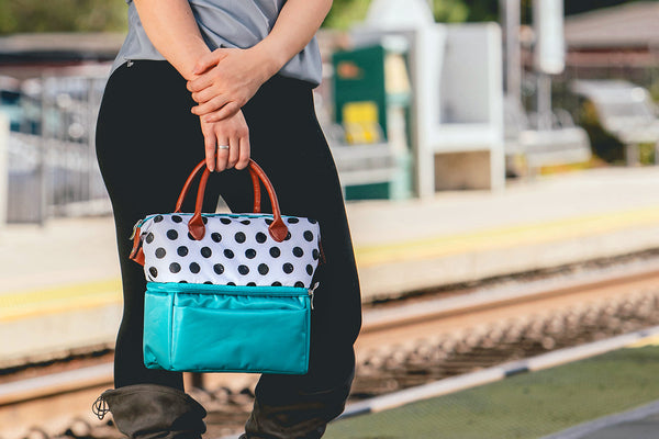Person holding a polka dot insulated lunch bag while standing at a train station platform.