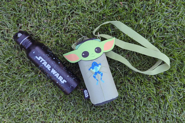 Star Wars water bottle and Grogu-themed shoulder pouch lying on green grass.