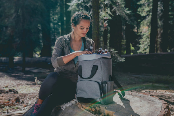 A woman sitting on a log, wearing a backpack, enjoying nature in a serene outdoor setting.