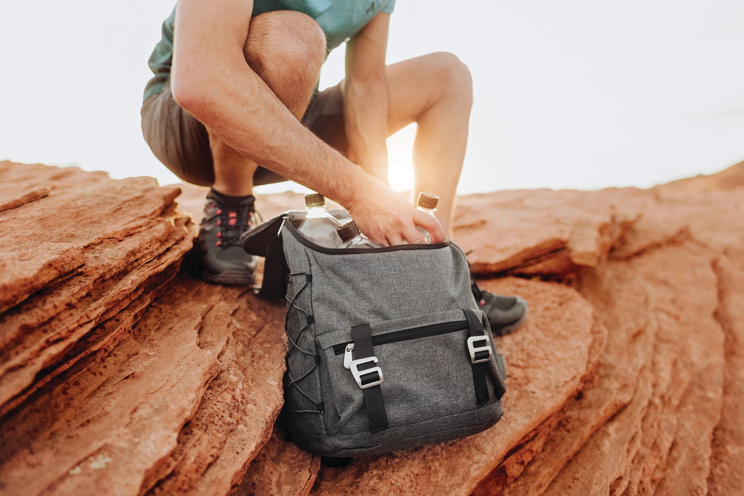 A man sits on a rock with a backpack beside him, enjoying the outdoors in a natural setting.