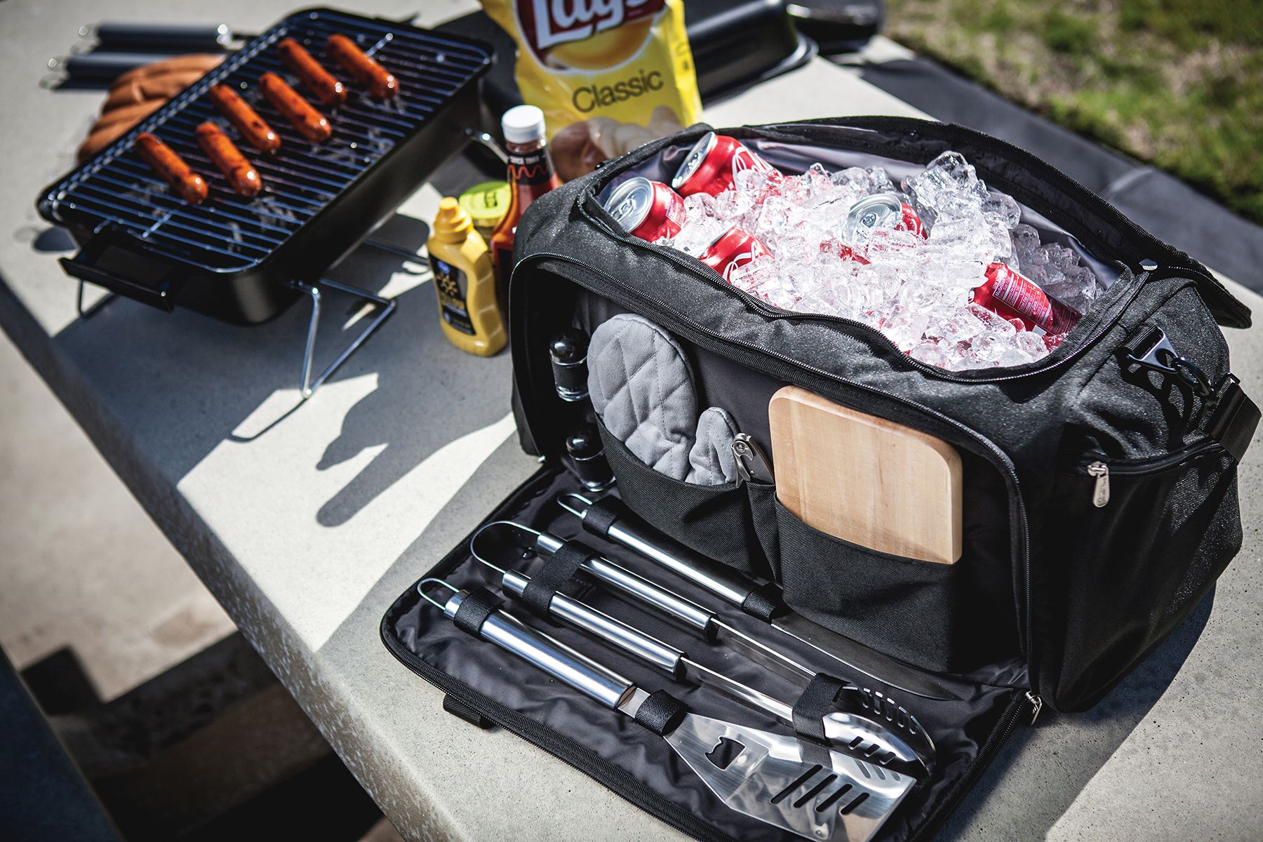 Grill bag containing hot dogs, BBQ tongs, and various grilling accessories for outdoor cooking.