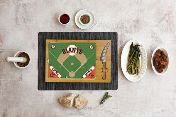 Baseball-themed cutting board with Giants field design, cheese knife, spices, bread, asparagus, and sausage sides.