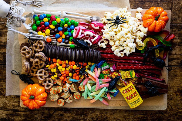 Halloween snack board with skeleton, pumpkins, popcorn, candy, pretzels, licorice, and gummy worms with toy spiders