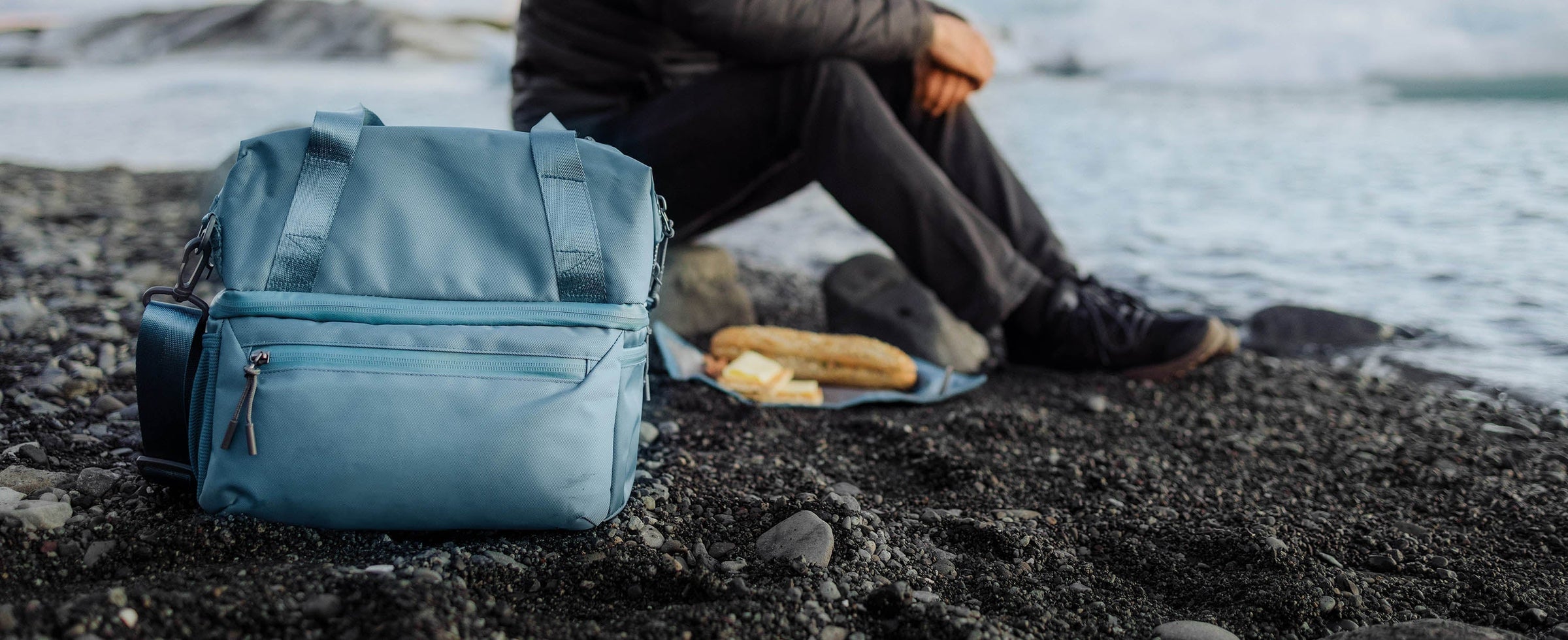 A man sits on the beach with a backpack, gazing at the ocean under a clear blue sky.