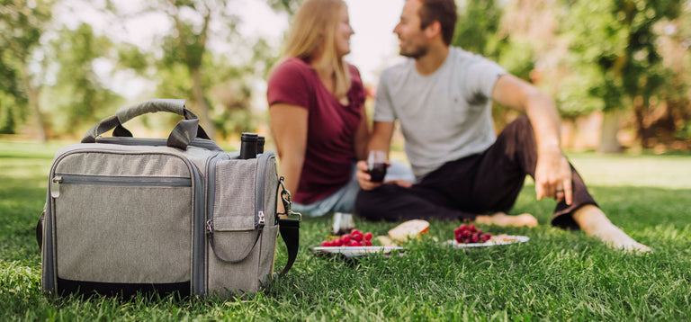 couple sitting on grass having a picnic with insulated picnic cooler bag