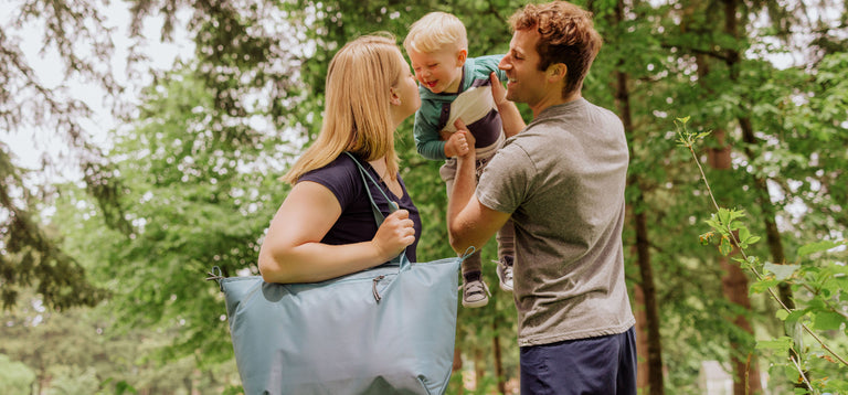 mom holding insulated cooler bag while dad plays with his young son while out on a hike