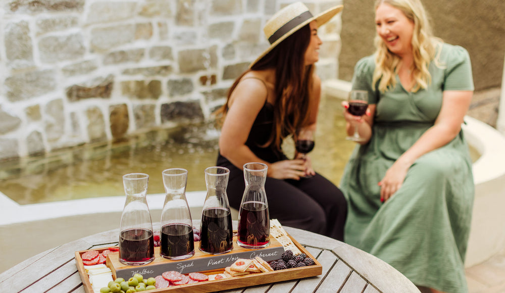 two women having a glass of wine and chatting with a wine sampler and snacks sitting on a table near them