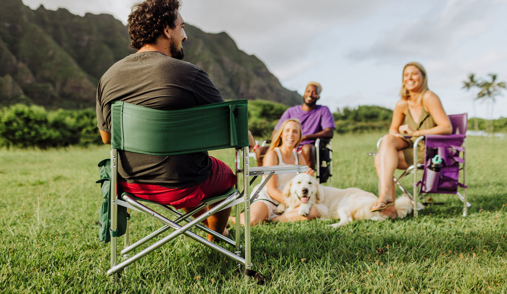group of friends sitting together in outdoor sports camping chairs with a dog laying in the grass