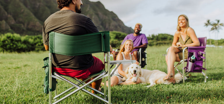 group of friends sitting together in outdoor sports camping chairs with a dog laying in the grass