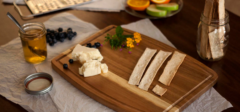 cutting board on table with cheese, crackers, fruit and honey
