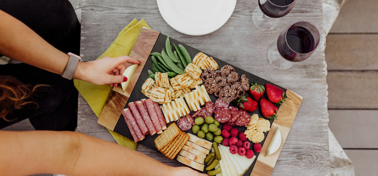 woman placing slate and acacia charcuterie board on the table with two glasses of wine