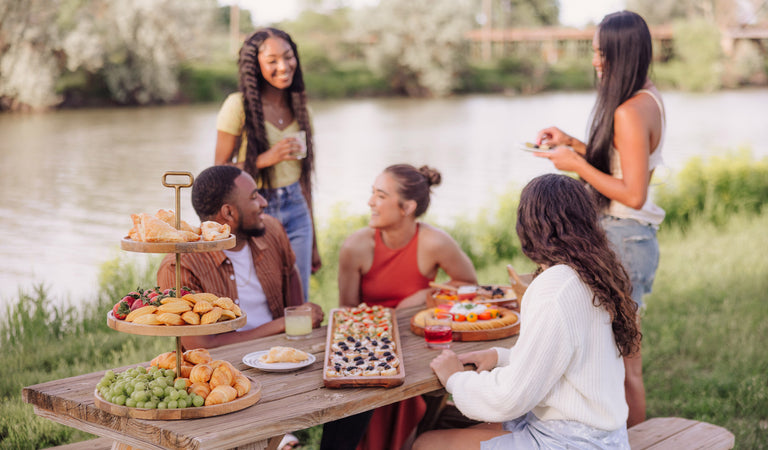 A group of people enjoying a meal together at a picnic table filled with various foods and drinks.